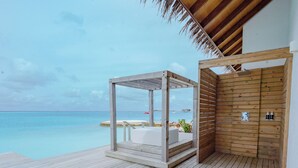 Une terrasse en bois avec un espace salon fermé par des baies vitrées, offrant une vue sur l’océan.