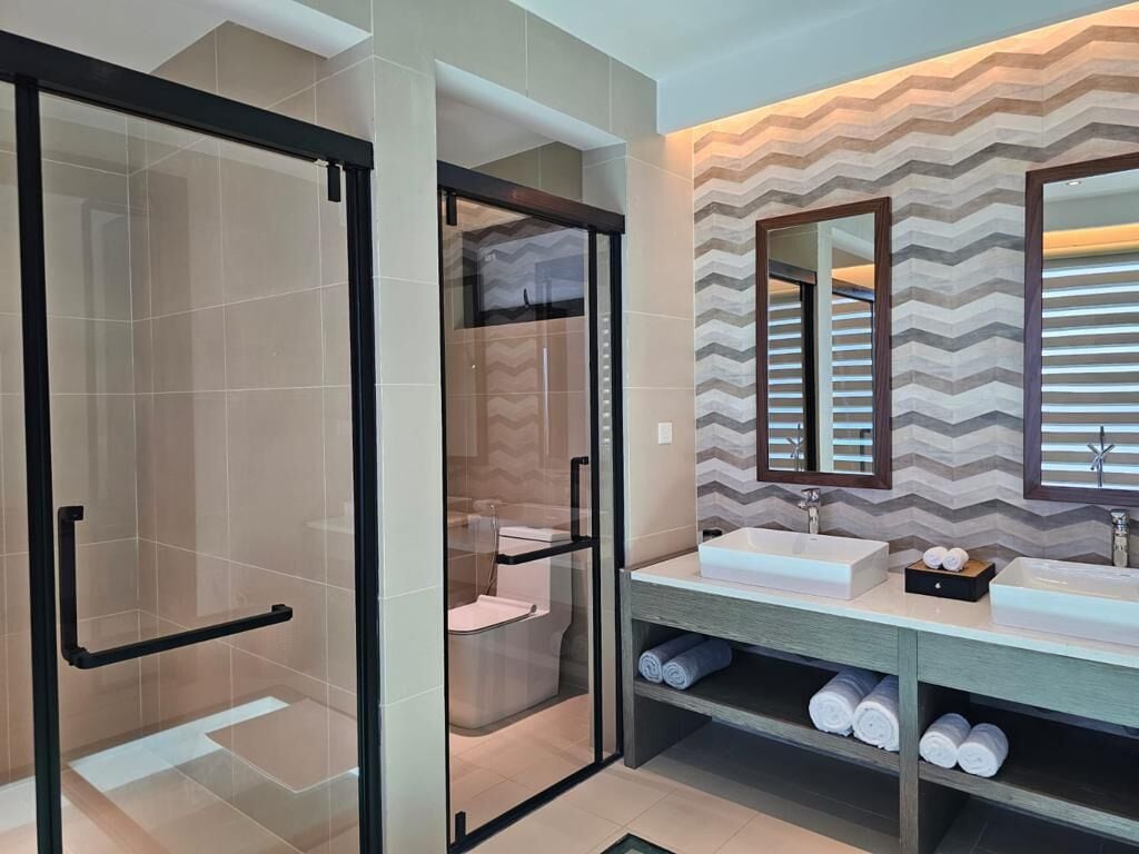 A modern bathroom with a glass shower enclosure, a vanity with a large mirror, and a chevron-patterned wall.