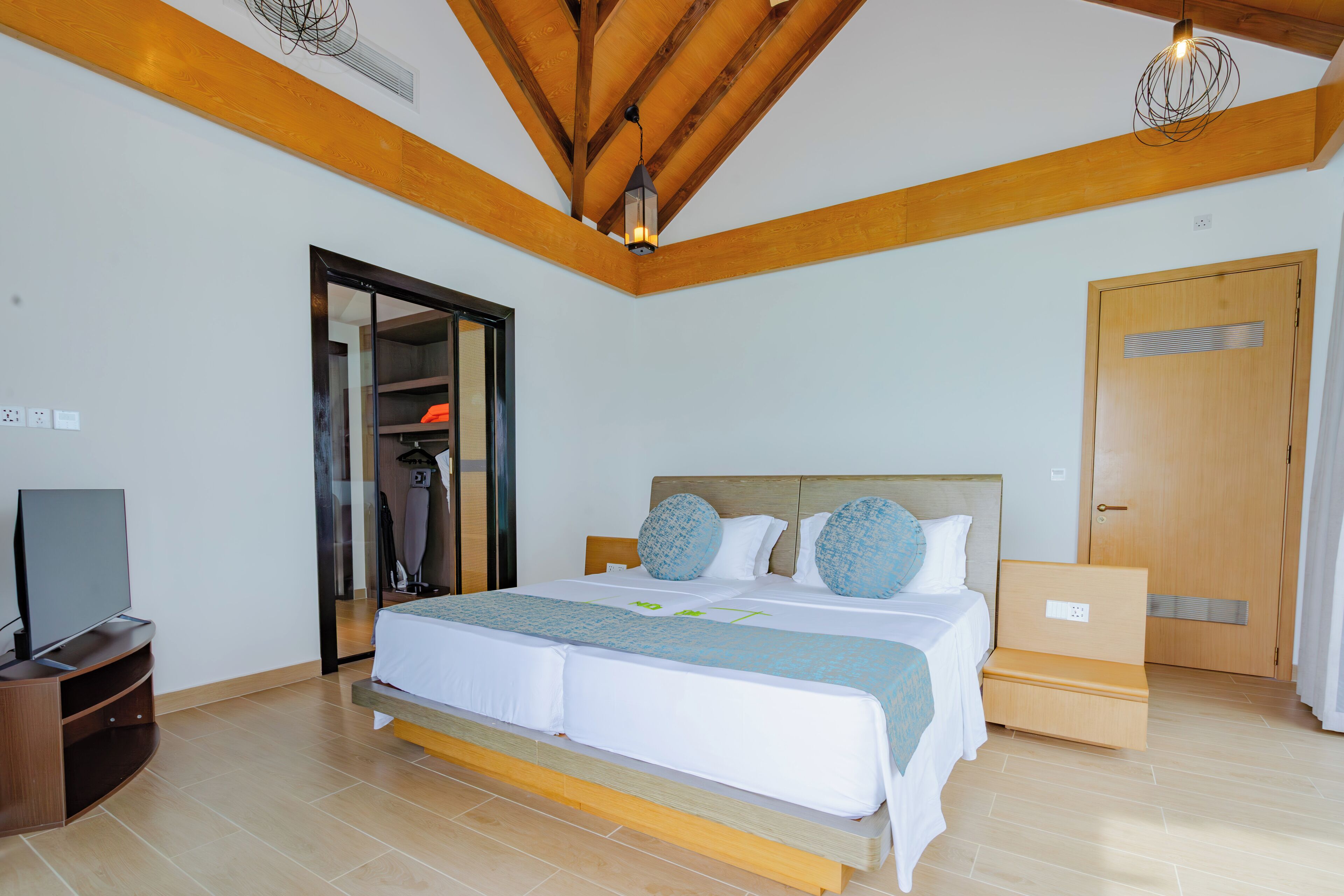 A modern bedroom with a large bed, wooden beams, a television, and a wardrobe.