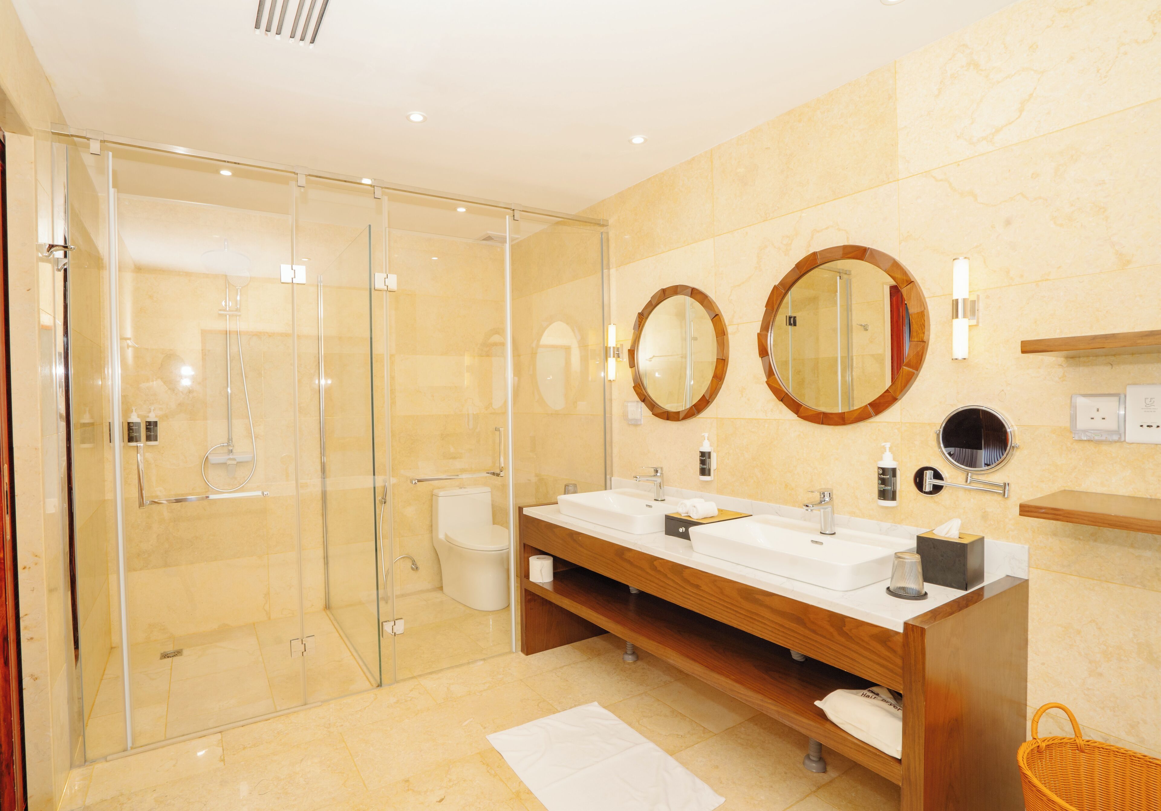 Une salle de bain moderne dotée d’une douche à parois de verre, de deux lavabos et d’un meuble-lavabo en bois.