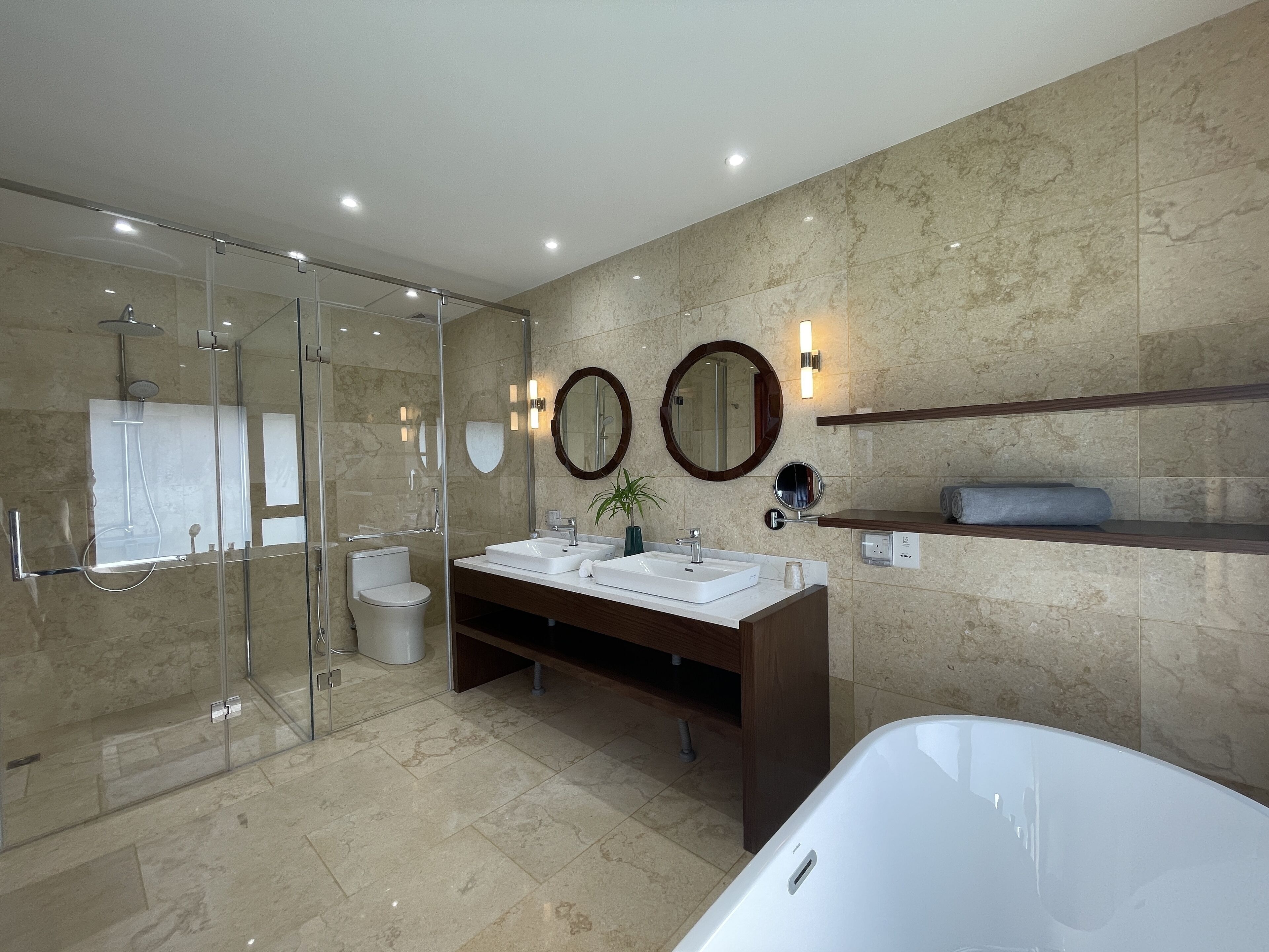 A modern bathroom with a glass-enclosed shower, a white bathtub, and a vanity with two sinks.