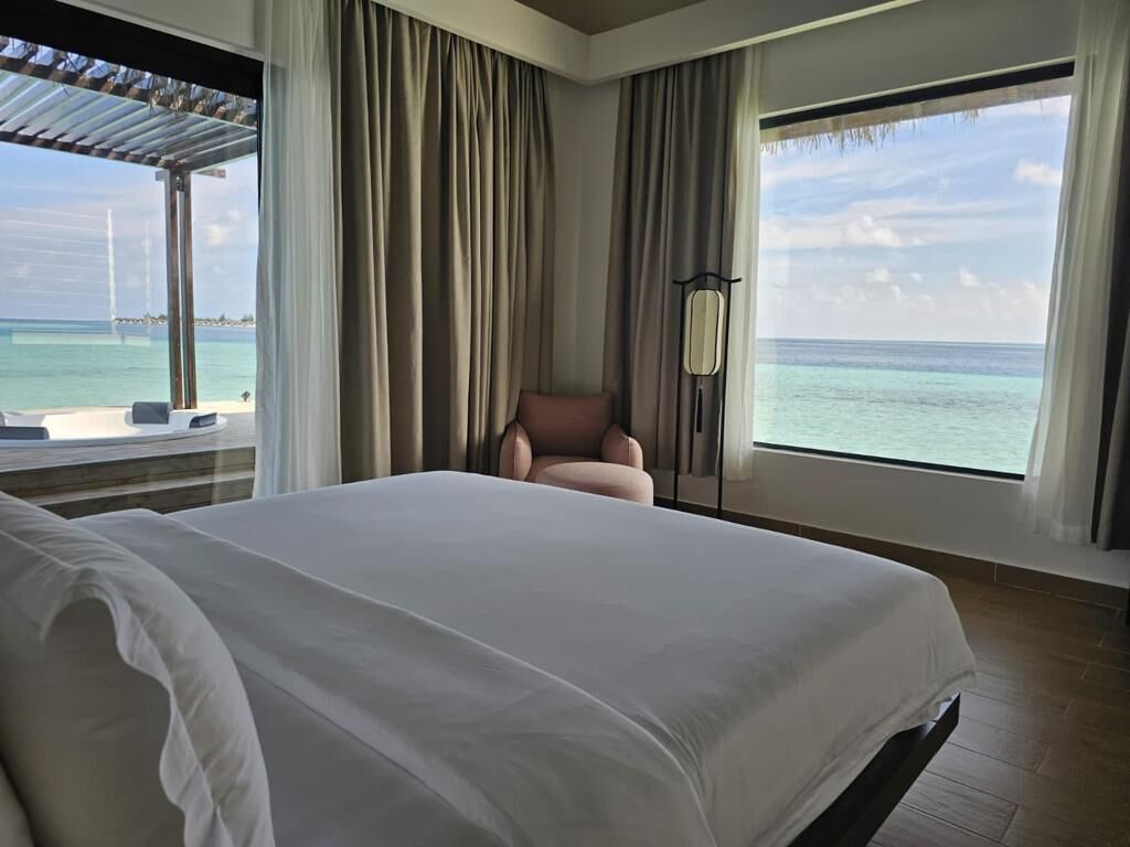 A hotel room with a large bed, a chair, and a view of the ocean.