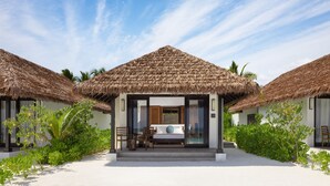 Un bungalow situé en bord de mer, doté d’un toit de chaume, d’un balcon et d’une vue sur l’océan.