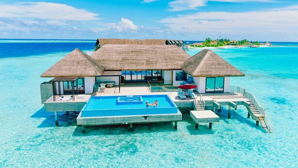 Un bungalow sur pilotis doté d’une piscine, de structures à toits de chaume et offrant une vue dégagée sur l’océan.