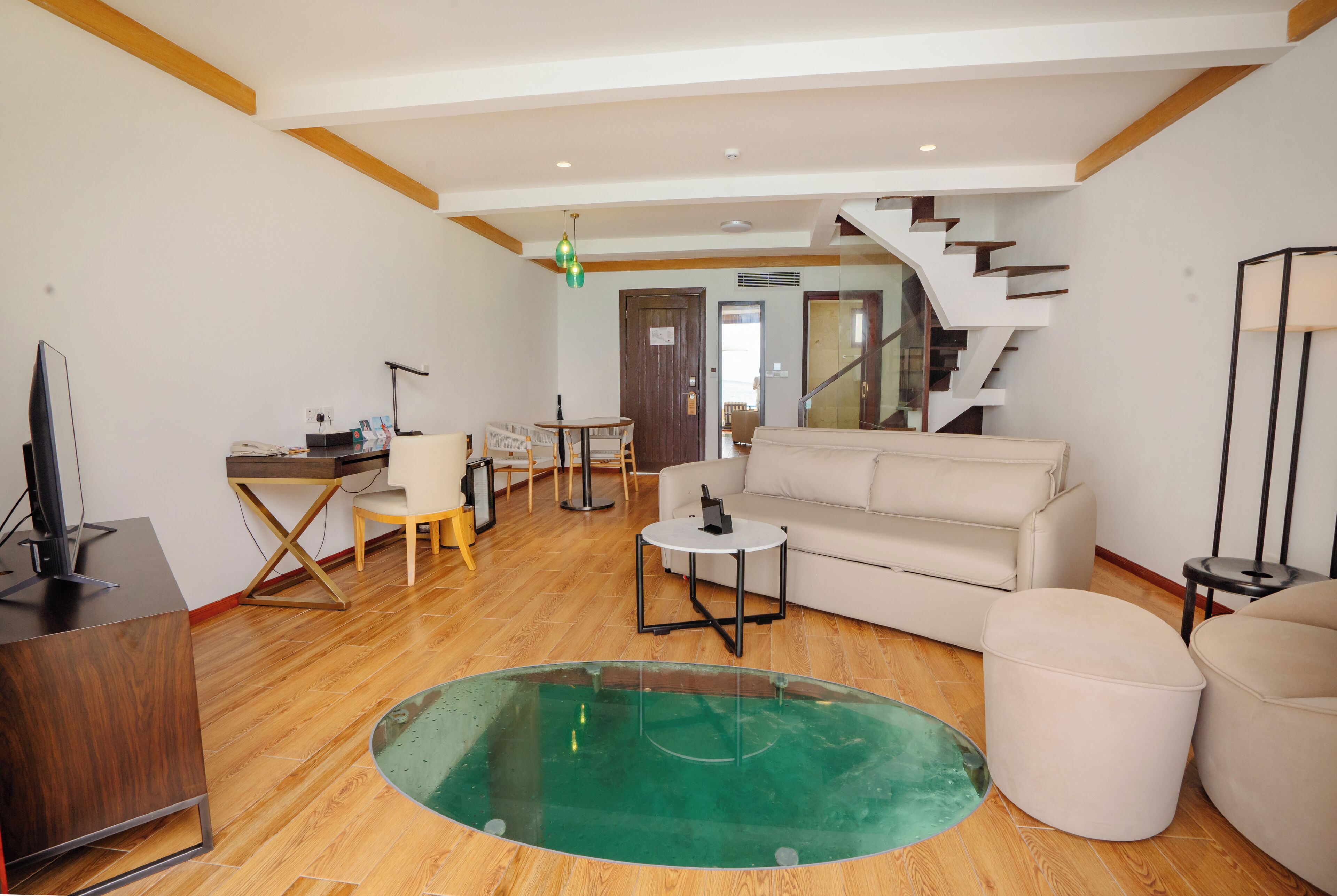 A spacious living area with a wooden floor, a round glass coffee table, a sofa, and a staircase leading to another level.