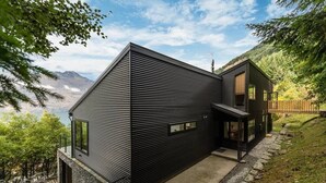 A modern two-story house with a sloped roof, large windows, and a stone foundation. - Large Pure Alpine Privacy and Recently Renovated (Queenstown)