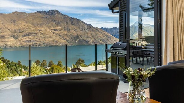 A balcony with a view of a lake and mountains, a grill, and a vase with flowers. - Large Pure Alpine Privacy and Recently Renovated (Queenstown)