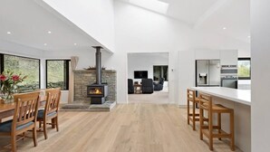 A modern kitchen with a central island, a dining area with wooden chairs, and a stone fireplace. - Large Pure Alpine Privacy and Recently Renovated (Queenstown)