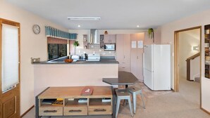 Kompakti keittiö, jossa on keskeinen saareke, ruokapöytä ja jääkaappi.