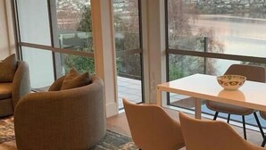 A modern room with large windows, a dining table with chairs, and a comfortable seating area. - Ultimate Views - Tikumu Lake House (Queenstown)