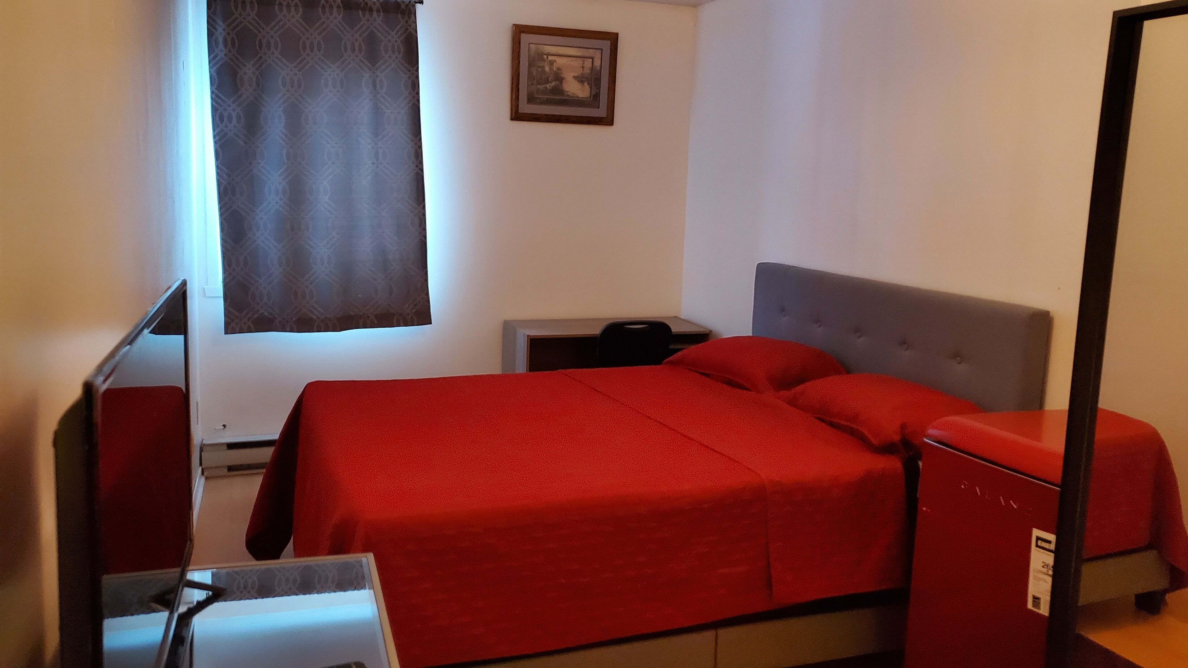 Quarto com cama, escrivaninha, cadeira, mesa de cabeceira e janela com cortina.