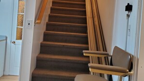 Een bekleedde trap met een leuning, een stoel onderaan en een deur met een decoratief paneel.