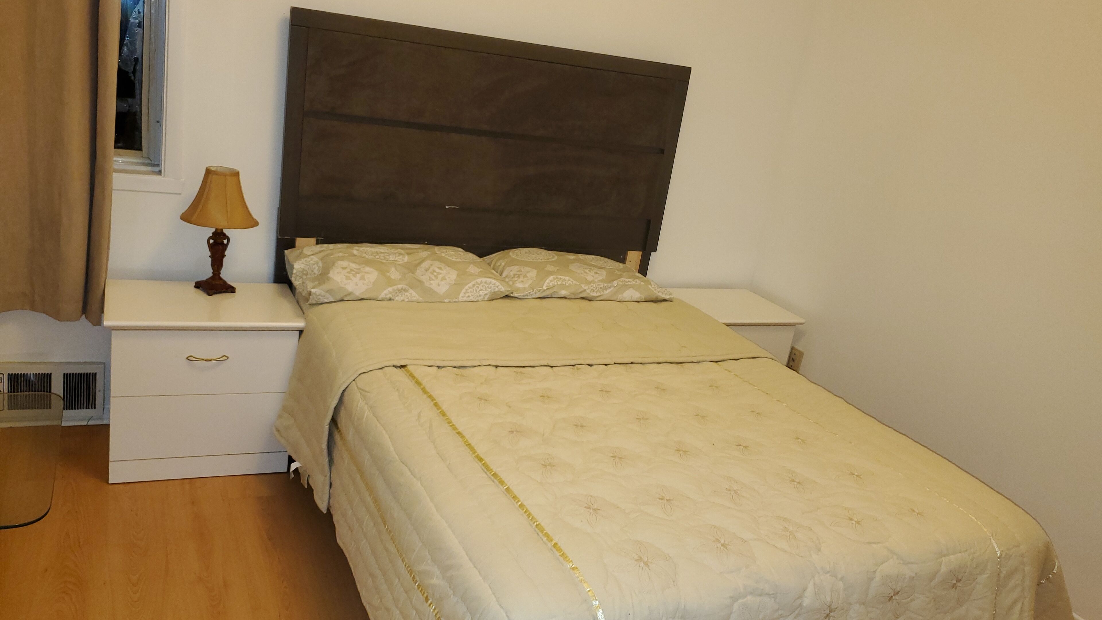 Un dormitorio con cama, mesitas de noche, lámpara y ventana.