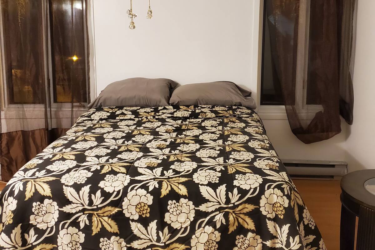 Une chambre à coucher avec un lit, deux oreillers, un ventilateur de plafond et des rideaux.
