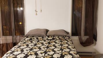 Een slaapkamer met een bed, twee kussens, een plafondventilator en gordijnen.