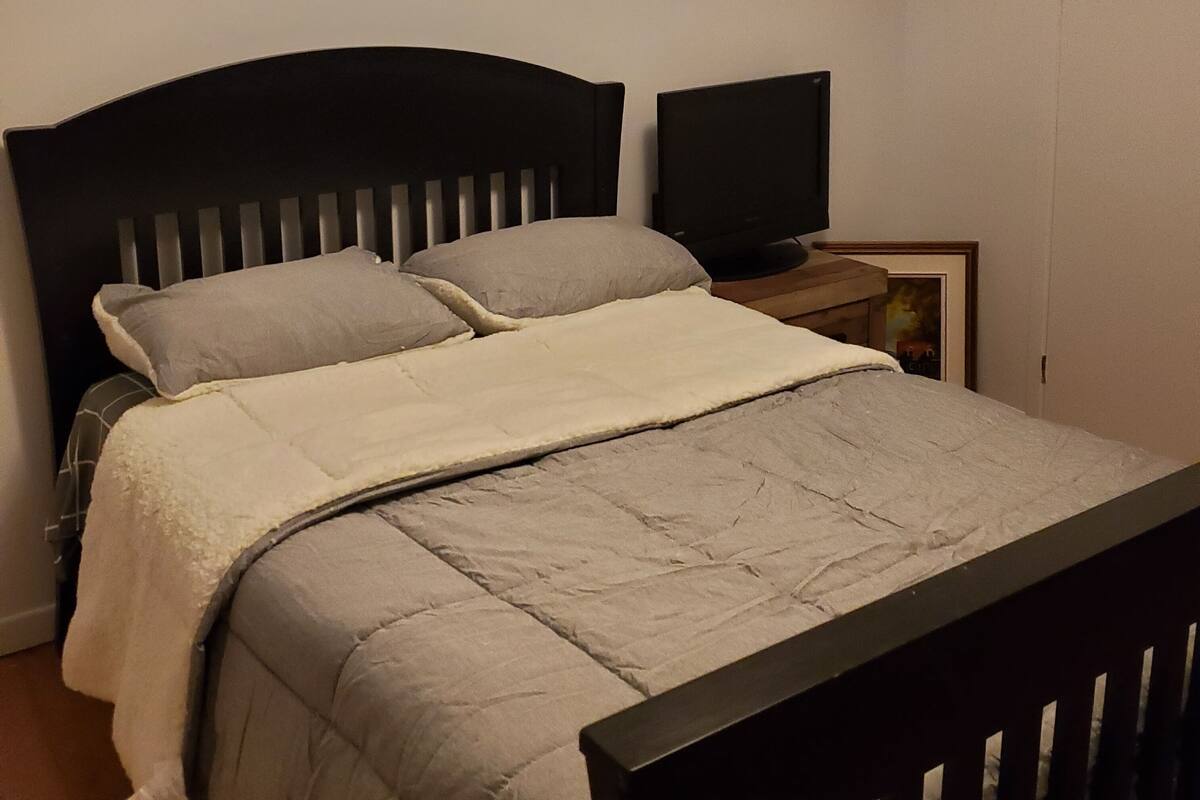 Un lit simple avec une tête de lit, une table de chevet avec une télévision et un tableau encadré au mur.