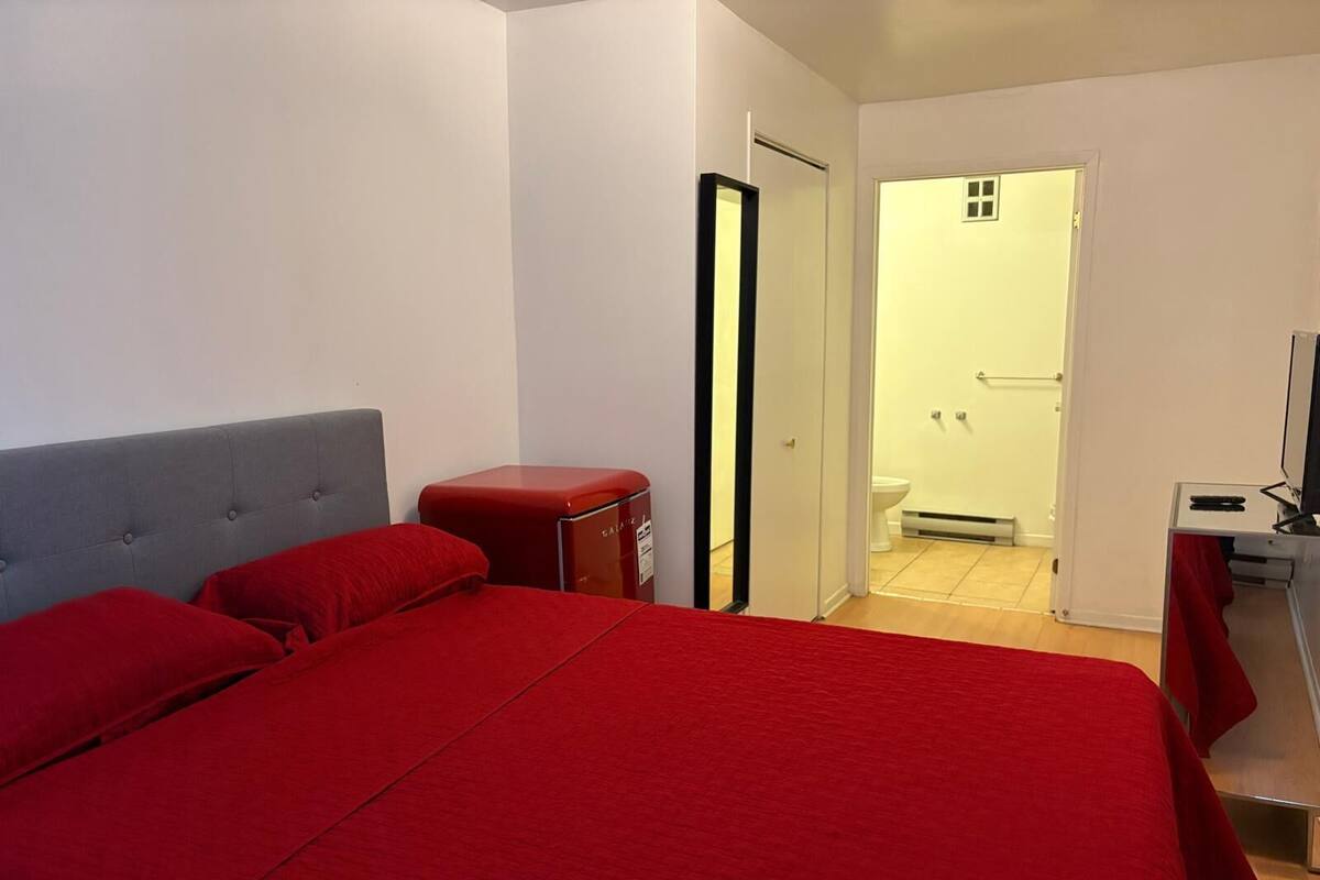 Une chambre d’hôtel avec un grand lit, une petite armoire rouge, une télévision et une salle de bain visible à travers une porte ouverte.