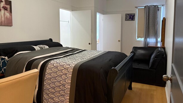 Een slaapkamer met een bed, een stoel, een deur en een raam met gordijnen.