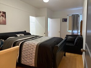 Une chambre à coucher avec un lit, une chaise, une porte et une fenêtre avec des rideaux.
