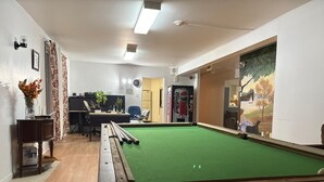 Een biljartkamer met een biljarttafel, een bureau met een computer en een groot raam met uitzicht op een park.