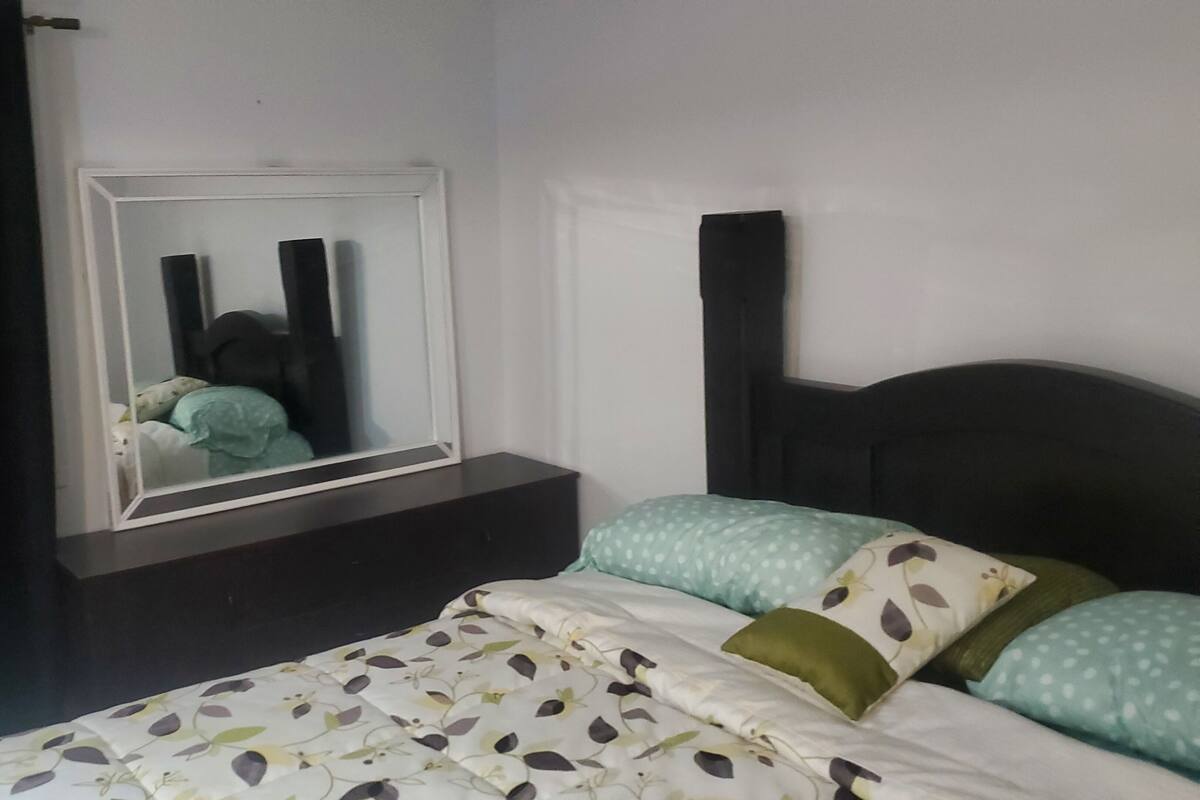 Une chambre à coucher avec un lit, une table de chevet, un miroir et une fenêtre avec des rideaux.