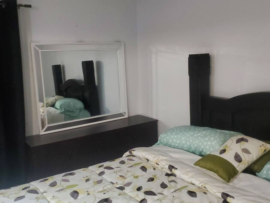 Un dormitorio con cama, mesita de noche, espejo y ventana con cortinas.