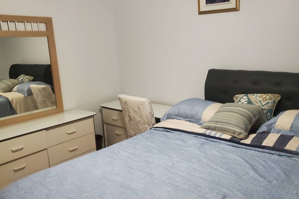 Une chambre à coucher comprenant un lit, une commode, une table de chevet, un miroir et un tableau encadré accroché au mur.