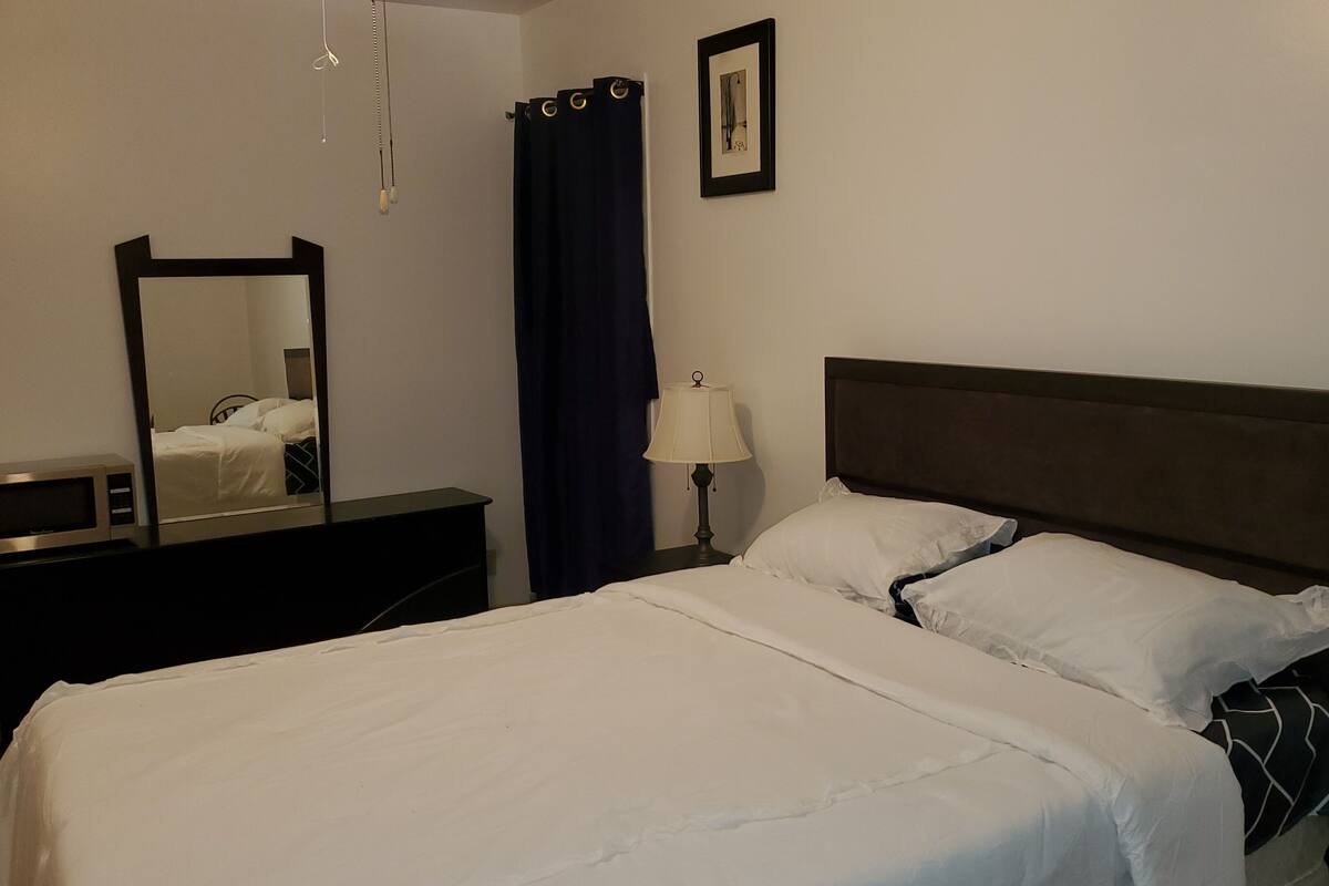 Une chambre d’hôtel avec un lit, une table de chevet, une lampe, un miroir et un tableau au mur.