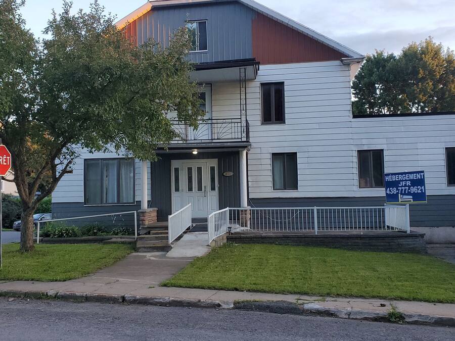 Un edificio residencial de dos pisos con entrada principal, buzón a la vista y una señal de parada.