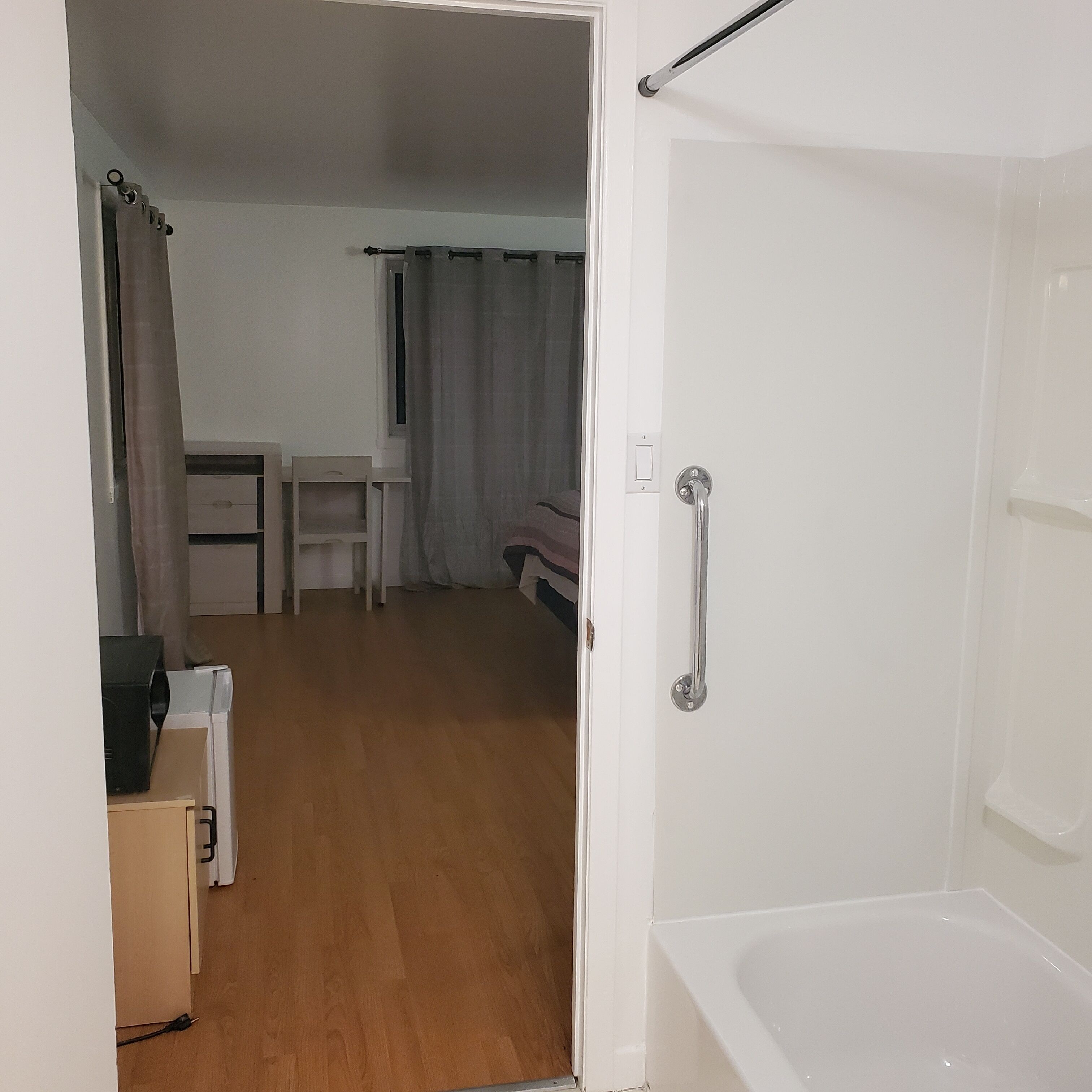 Una habitación con piso de madera, una bañera blanca, un escritorio, una silla y una cama.