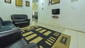 A living room with a black leather sofa, a patterned rug, and a television mounted on the wall. - OYO HOME 90646 Casaria Paka Homestay (Dungun)