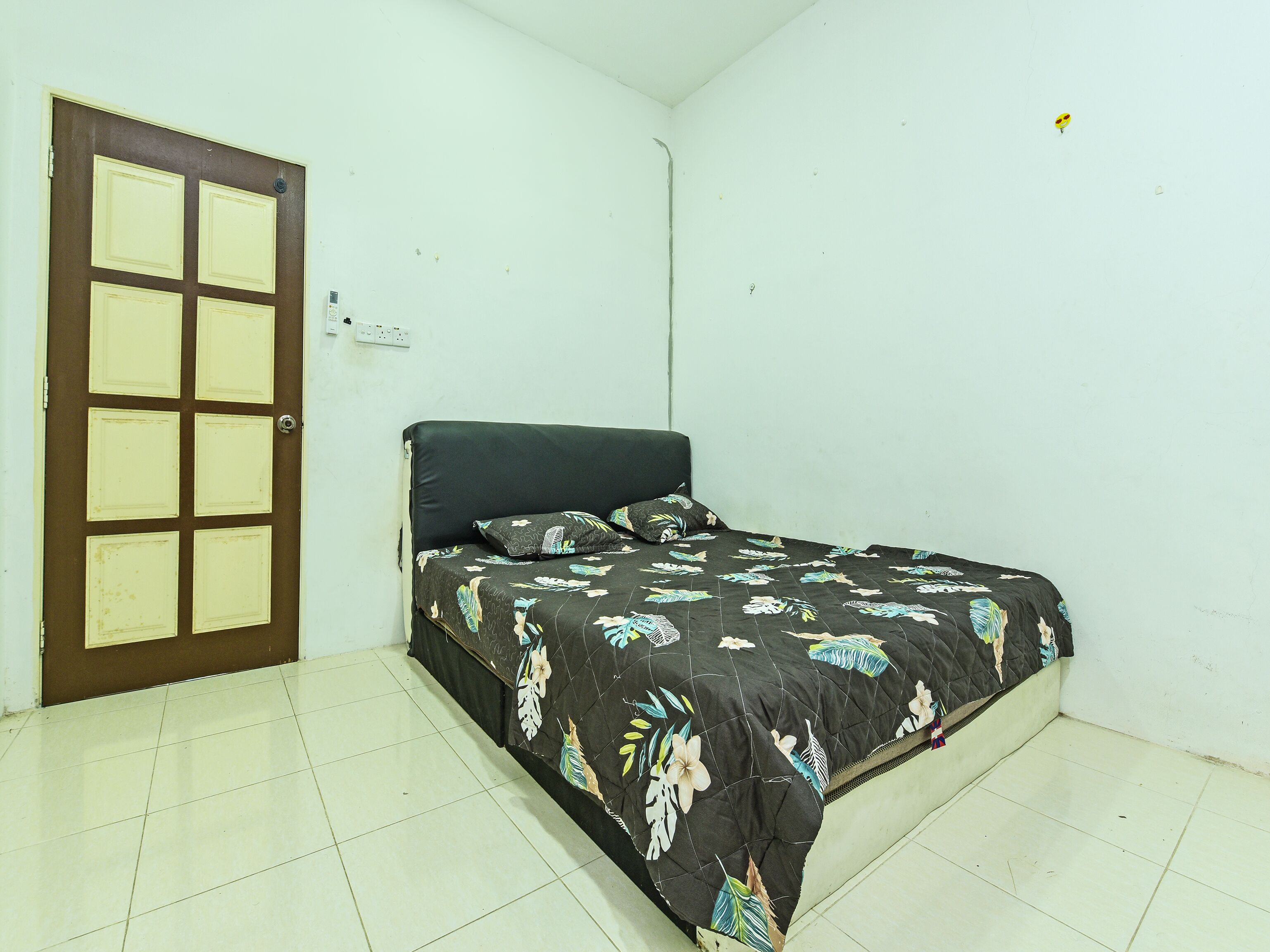 A small, clean room with a single bed, a door with a grid pattern, and white walls.