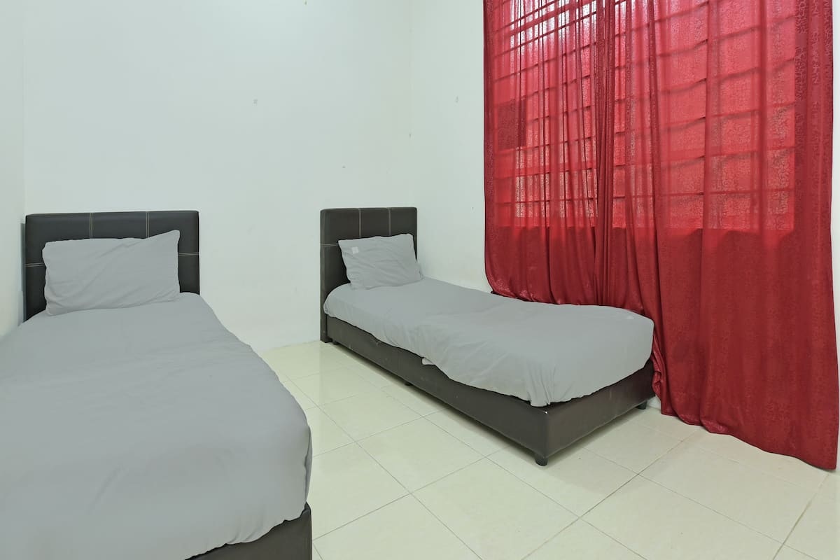 Dos camas individuales con ropa de cama gris en una habitación con suelo de baldosas blancas y una cortina roja.