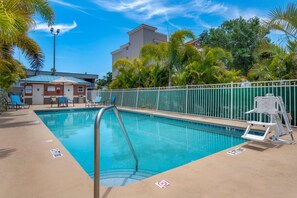 A swimming pool with a metal ladder, surrounded by a green fence, and a building with a sign in the background. - Comfort Inn & Suites Melbourne Viera (Melbourne)
