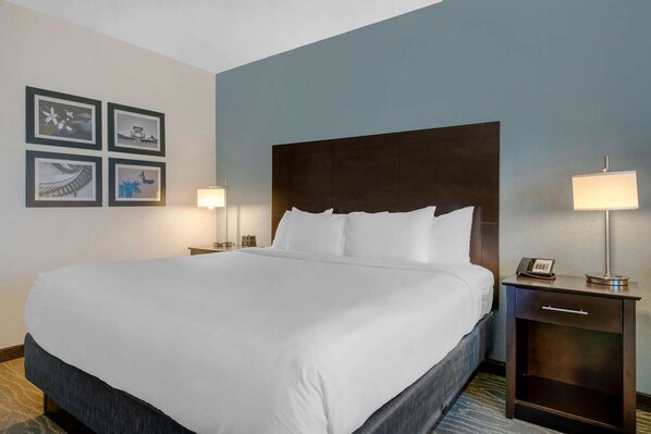 A hotel room with a large bed, two bedside tables, a nightstand, and a wall with framed pictures. - Comfort Inn & Suites Melbourne Viera (Melbourne)
