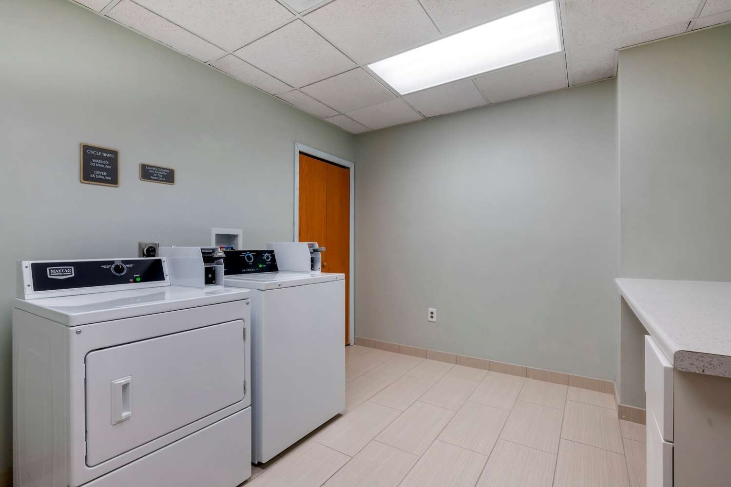 A laundry room with two Maytag washers and dryers, a wooden door, and a tiled floor.