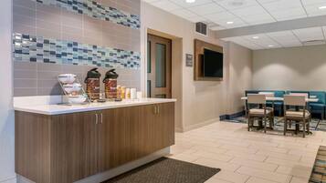 A hotel lobby with a reception desk, a coffee station, seating area, and a television mounted on the wall.