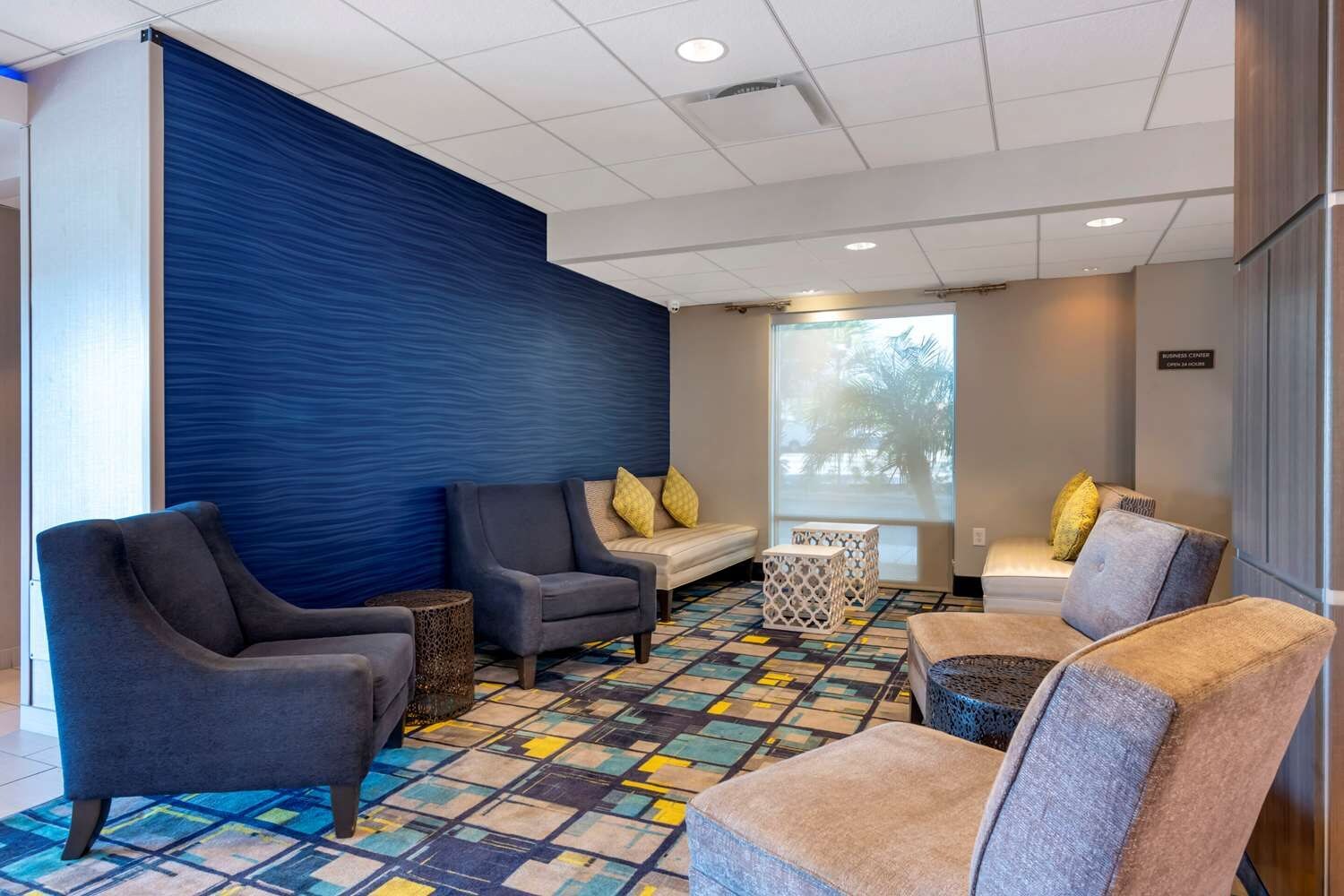 A modern lounge area with sofas, a patterned carpet, and a large window with a view.