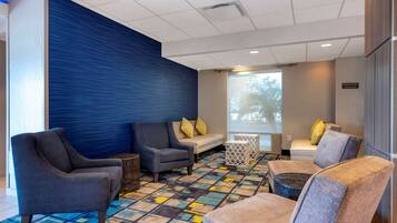 A modern lounge area with sofas, a patterned carpet, and a large window with a view.