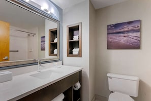 A bathroom with a large mirror, two wooden shelves with towels, a toilet, and a painting of a beach scene. - Comfort Inn & Suites Melbourne Viera (Melbourne)