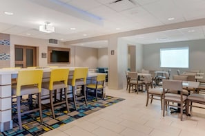 A modern dining area with a long table and chairs, a projector screen, and a tiled floor. - Comfort Inn & Suites Melbourne Viera (Melbourne)