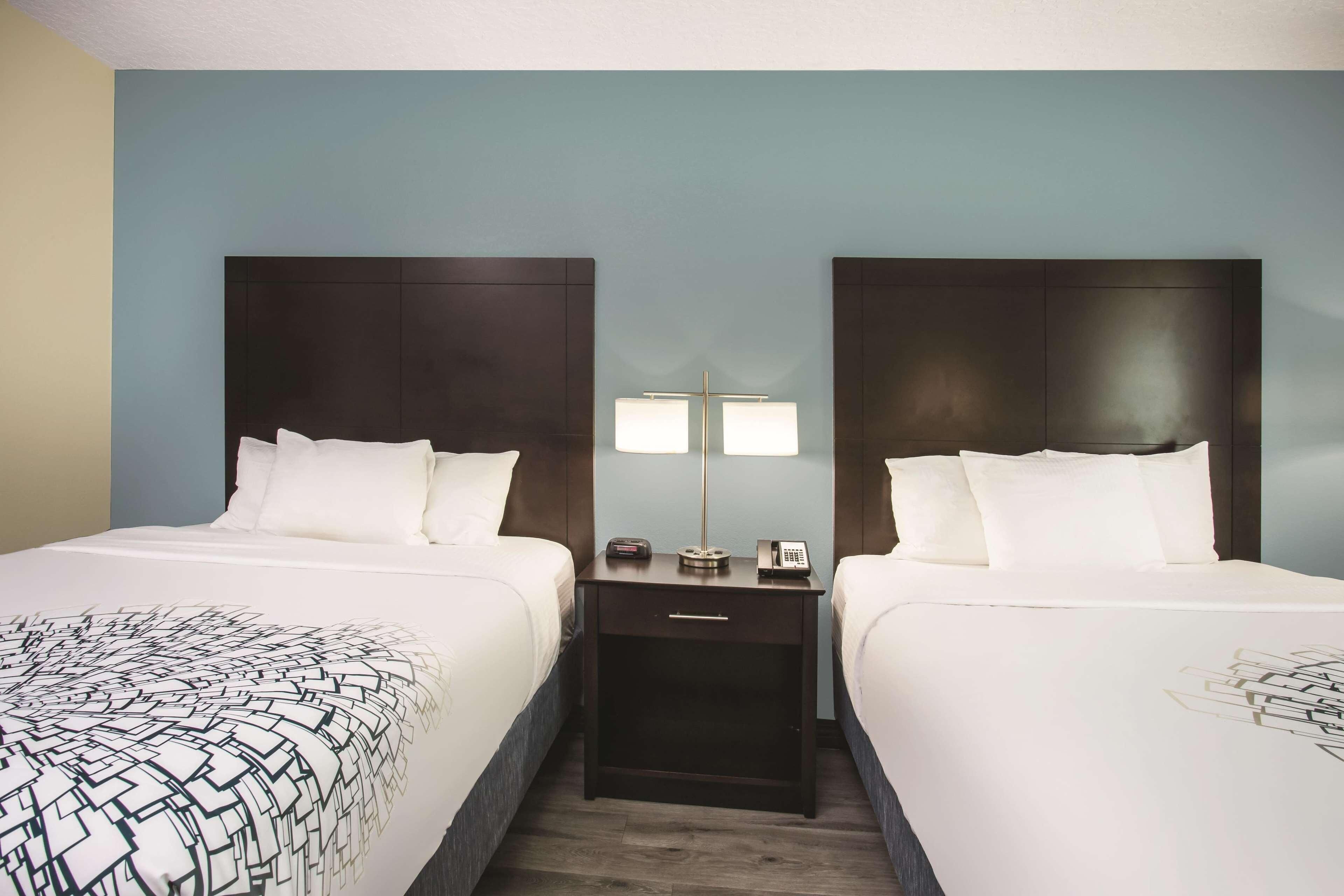 A hotel room with two beds, a nightstand with a lamp, and a phone.