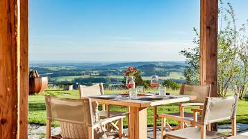 Ein Essbereich im Freien mit Holztisch und -stühlen, Blick auf sanfte Hügel und eine rustikale Holzkonstruktion.