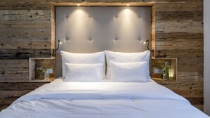 A neatly made bed with a wooden headboard, two bedside tables with lamps, and a small shelf with decorative items. - Gipfelglück-chalet-suite mit 60qm, Schlafzimmer, Wohnraum mit Küche und Bad mit Sauna (Frasdorf)
