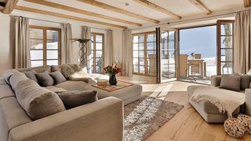 Ein geräumiges Wohnzimmer mit einer großen Couch, einem Couchtisch und Blick auf eine verschneite Landschaft durch große Fenster.