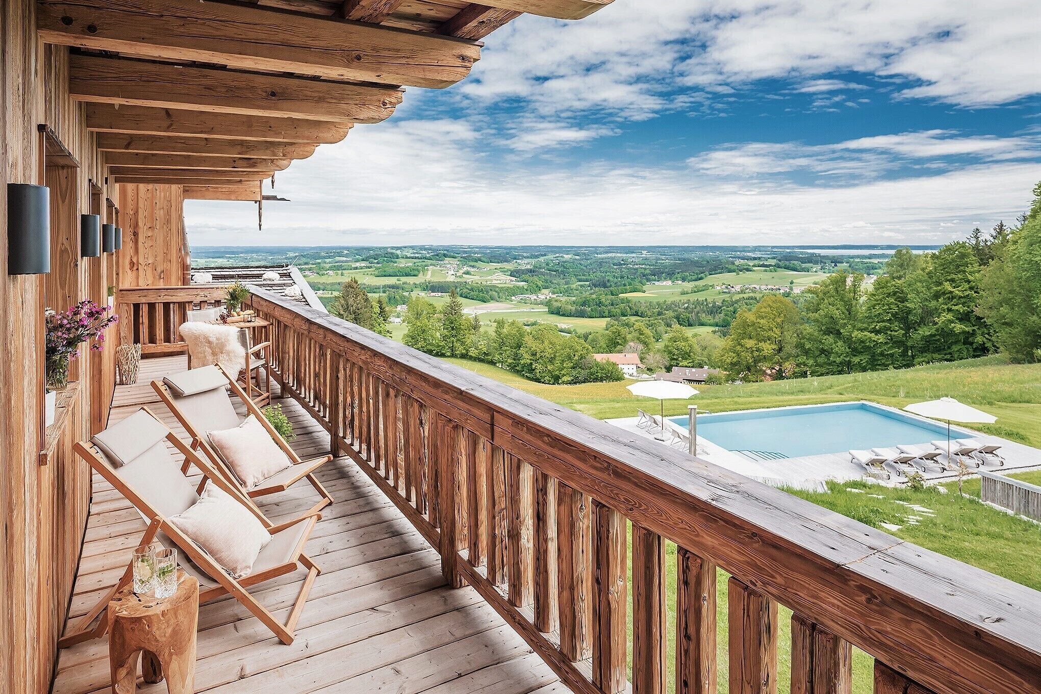 A wooden deck with lounge chairs and a view of a swimming pool and landscape.