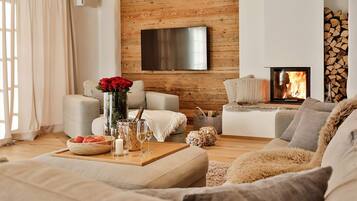 Ein gemütliches Wohnzimmer mit Kamin, einem an einer Holzwand montierten Flachbildfernseher und einer komfortablen Sitzecke mit Sofa und Sesseln.
