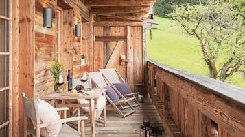 Eine Holzterrasse mit zwei Liegestühlen, einem Tisch mit einer Weinflasche und einer Vase mit Blumen.