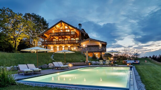 Ein großes, zweistöckiges Holzhaus mit Swimmingpool, Sitzgelegenheiten im Freien und einem gut beleuchteten Patio.