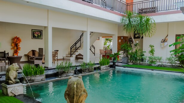 A pool area with a frog statue, indoor plants, and a staircase. - Dedy Beach Inn (Kuta)